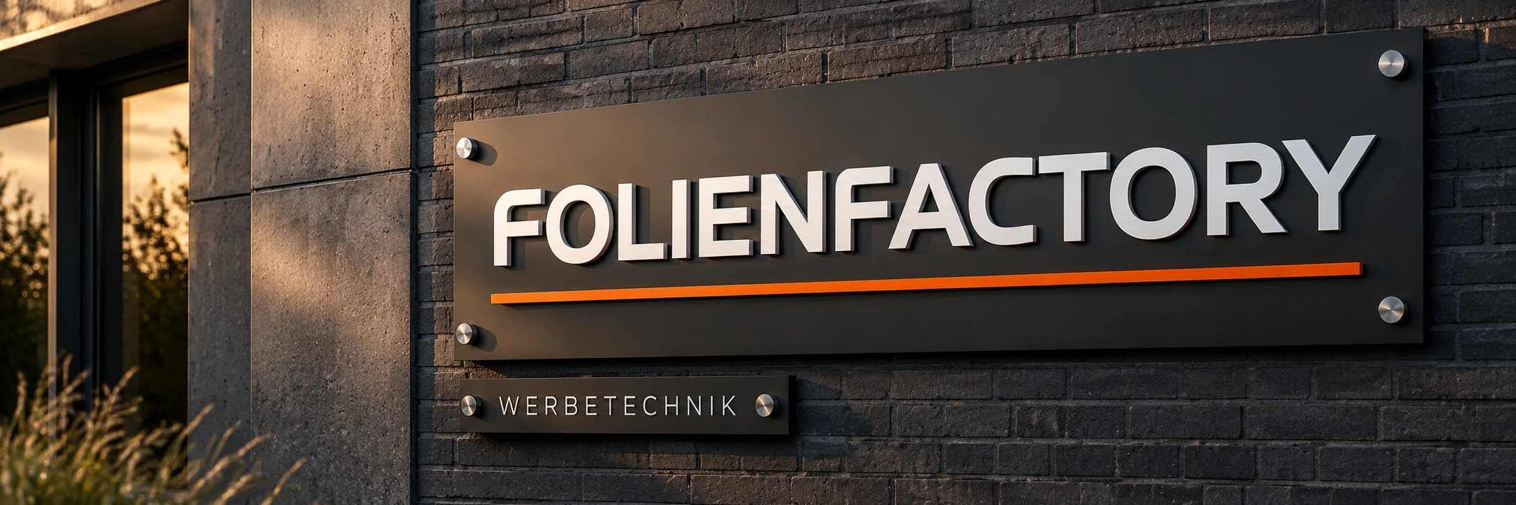 Gestaltungsbeispiel: anthrazitfarbenes FolienFactory-Firmenschild mit plastischen Buchstaben und orangefarbener Akzentlinie